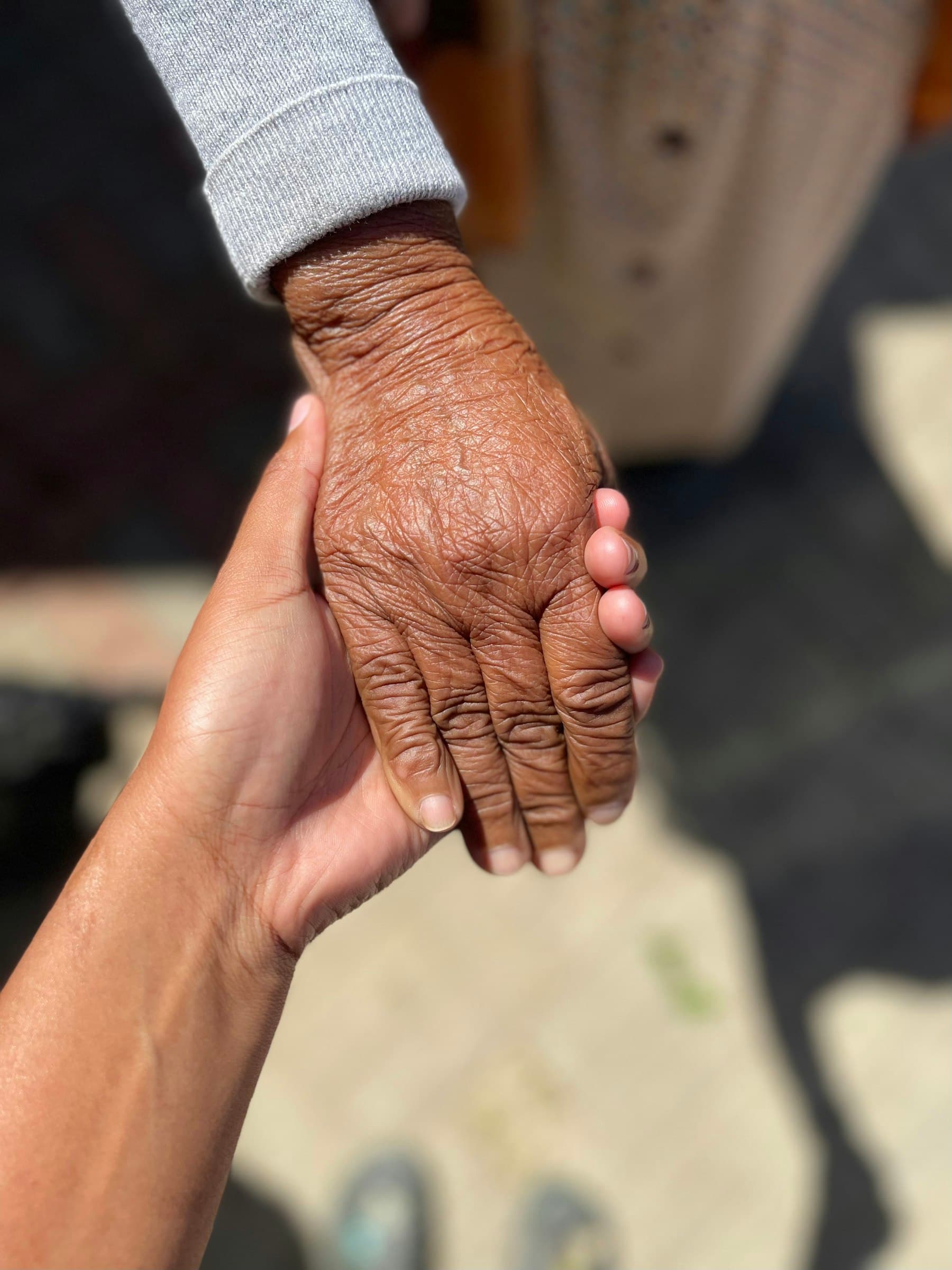 A young hand gently holding an elderly person's hand