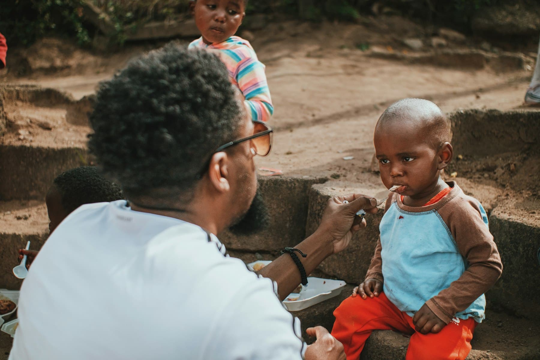 A volunteer kneeling to feed and care for a young child